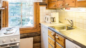A compact kitchen with wooden cabinets, a white stove, a coffee maker, and a sink. - Retkietappi honkapirtti by Interhome (Kuusamo)