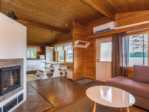 A cozy cabin interior with a fireplace, wooden walls, a dining area, and a sofa.