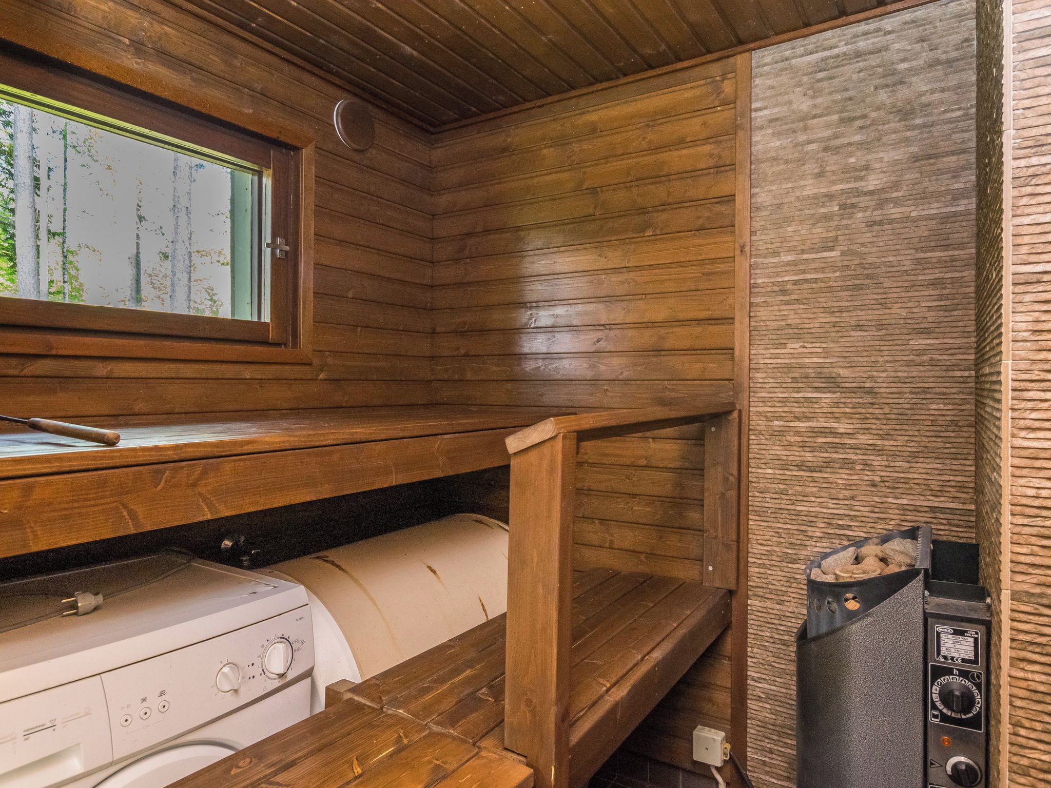 Eine kleine Küche mit Holzwänden, einem eingebauten Backofen und einem Fenster mit Blick auf Bäume.