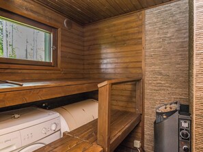 Une cuisine compacte aux murs en bois, dotée d’un four encastré et d’une fenêtre donnant sur les arbres.