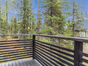 Eine Holzterrasse mit Geländer, mit Blick auf ein bewaldetes Gebiet mit hohen Bäumen.