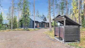 Mökki, jossa on maalaishenkinen tunnelma, sorapäällysteinen ajotie ja korkeiden mäntyjen muodostama suojaisa ympäristö.