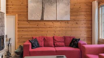 Ein gemütliches Wohnzimmer mit einem roten Sofa, einem Couchtisch und einem Baumgemälde an der Wand.