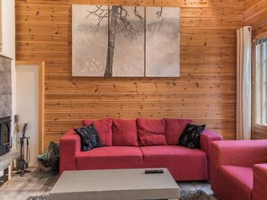 Ein gemütliches Wohnzimmer mit einem roten Sofa, einem Couchtisch und einem Baumgemälde an der Wand.