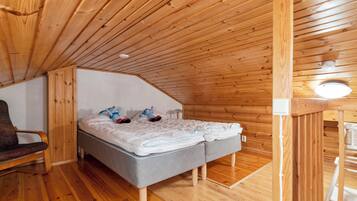 Una camera accogliente con soffitto spiovente, pareti in legno, un letto con cuscini e coperta, una sedia e un tavolino.