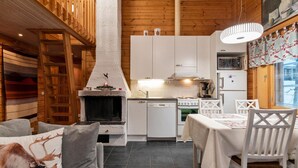 Interior acogedor de una cabaña con chimenea de piedra, paredes de madera, comedor y cocina.