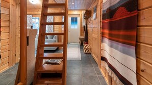 Interior de madera con una escalera de madera que lleva a una zona de altillo, una alfombra grande tejida y vistas al exterior a través de una ventana.