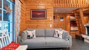 Interior acogedor de una cabaña con un sofá gris, paredes de madera, un cuadro enmarcado y una ventana con un adorno de estrella.