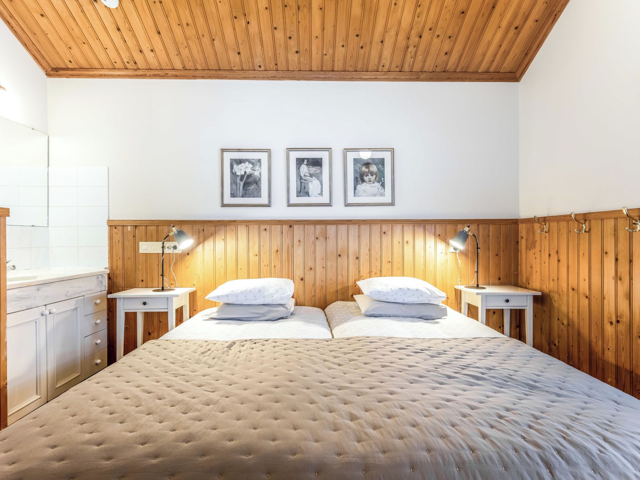 A bedroom with a wooden headboard, two bedside tables with lamps, a bed with a tufted headboard, and three framed pictures on the wall.