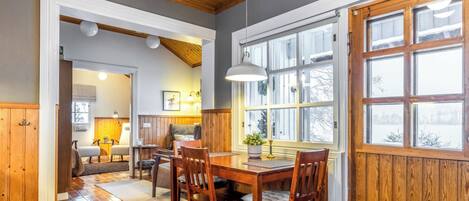 A dining area with a wooden table and chairs, a hanging light fixture, and a window with a view of the outdoors.