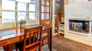 Ein gemütliches Zimmer mit einem Holzesstisch, Stühlen, einem Kamin und großen Fenstern.