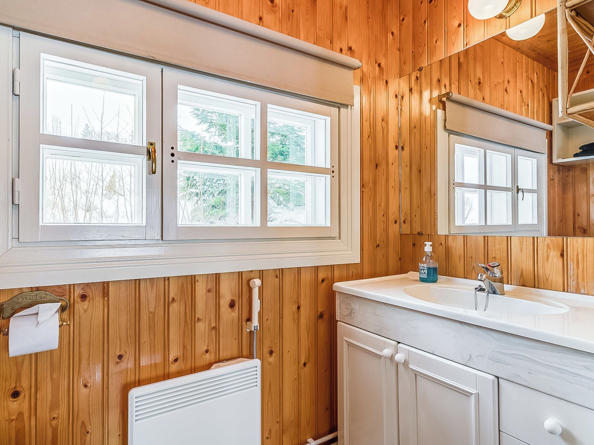 A bathroom with wooden paneling, a white sink, a mirror, and a window.