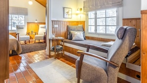 Ein gemütliches Blockhaus-Interieur mit Holzbalkendecke, einer Bank mit Kissen, einem Sessel und einem Fenster mit Blick auf Bäume.