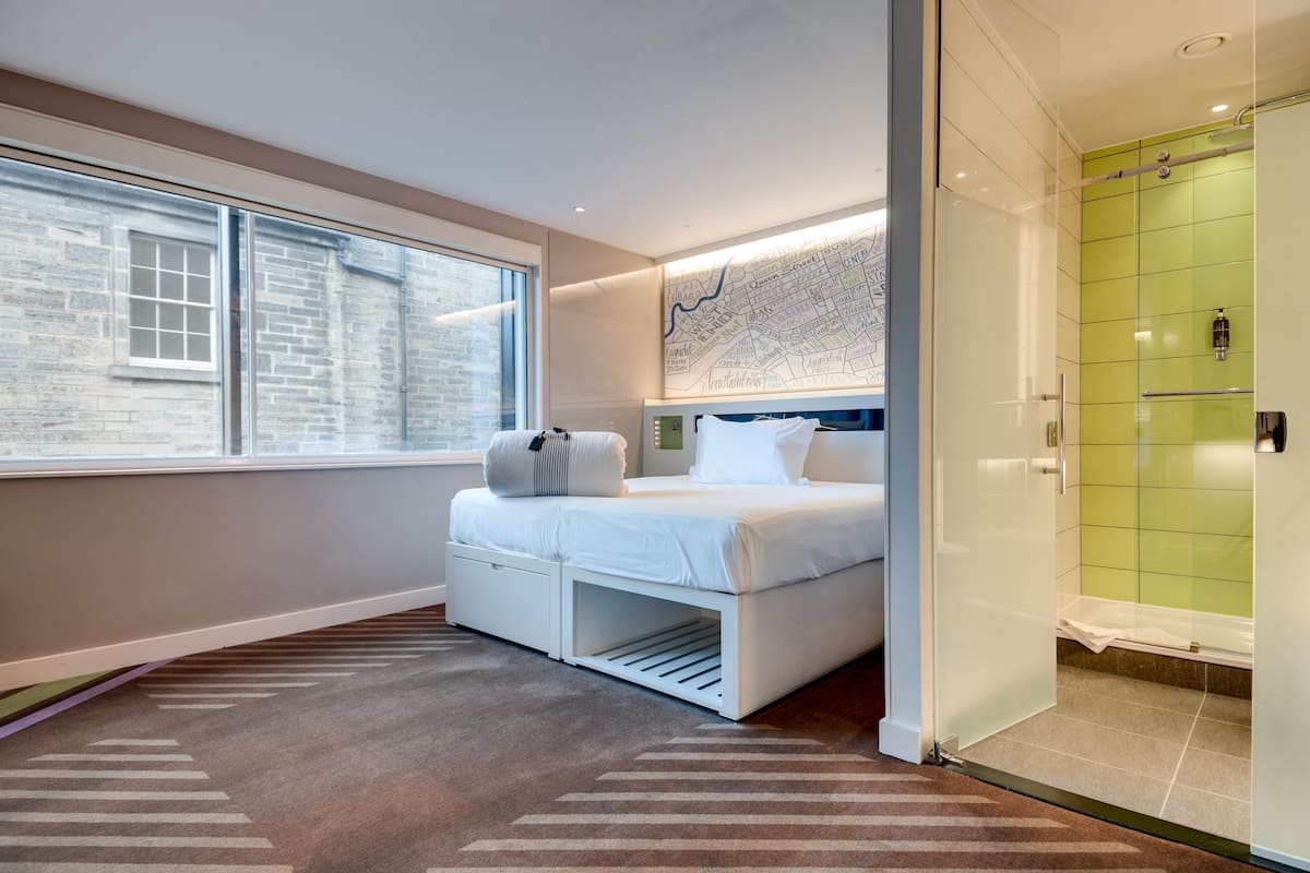 Quarto de hotel moderno com uma cama, um mapa na parede, uma janela e um espaço com chuveiro.