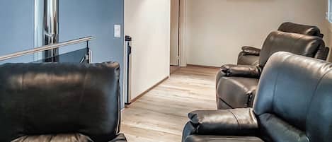 Quarto com dois sofás de couro, piso de madeira e parede branca com janela.