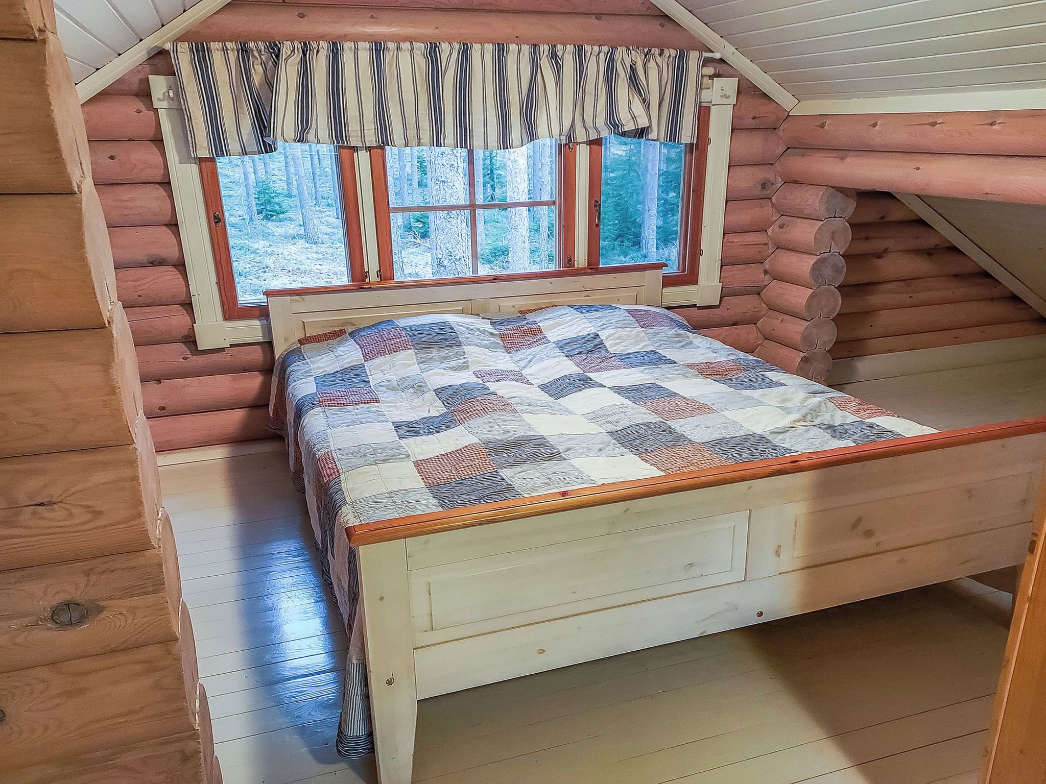 Quarto de cabana de madeira com cama, janelas e vista para uma paisagem nevada.