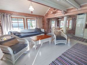 Interior d'una cabana de fusta amb un sofà, cadires, una taula i un frigorífic.