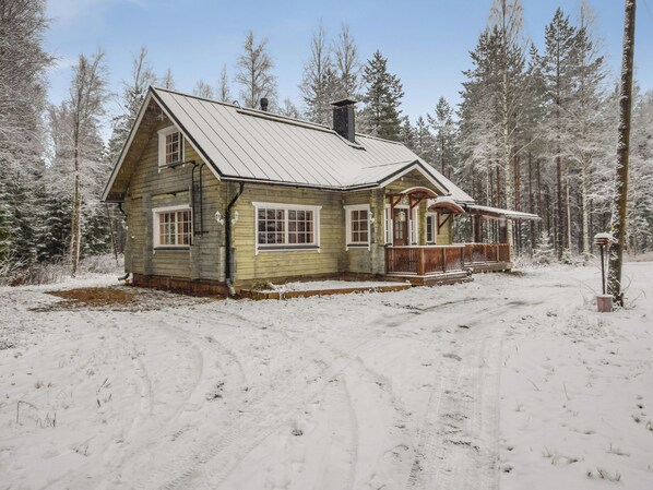 A wooden cabin with a porch, surrounded by a snowy forest.