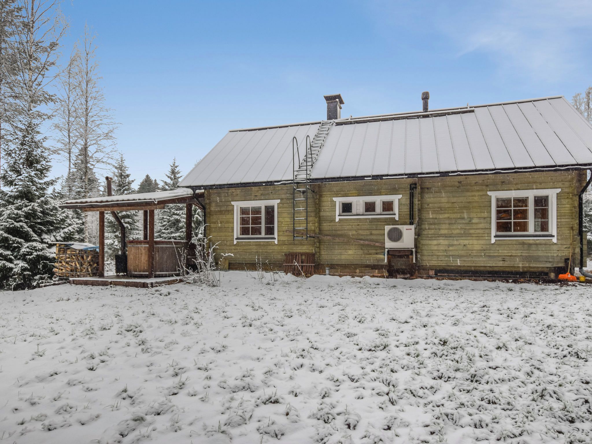 Una casa de madera con techo metálico, un porche cubierto y un patio cubierto de nieve.