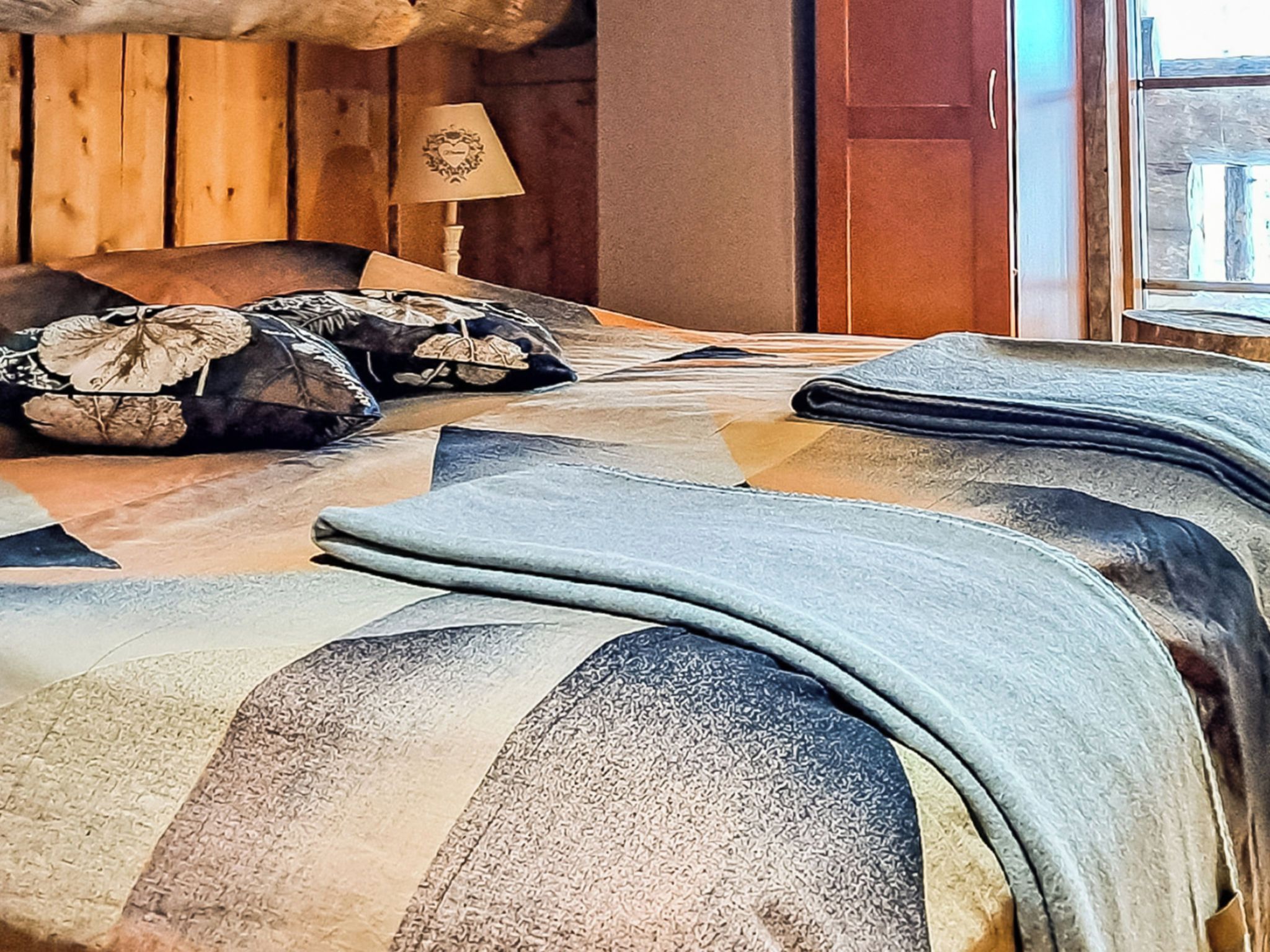 Een bed met een gestreept beddegoed en decoratieve kussens, een houten hoofdbord, een bedlamp en een deur op de achtergrond.