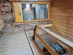 A wooden cabin with a small window, a wooden bench, and a fireplace with logs.