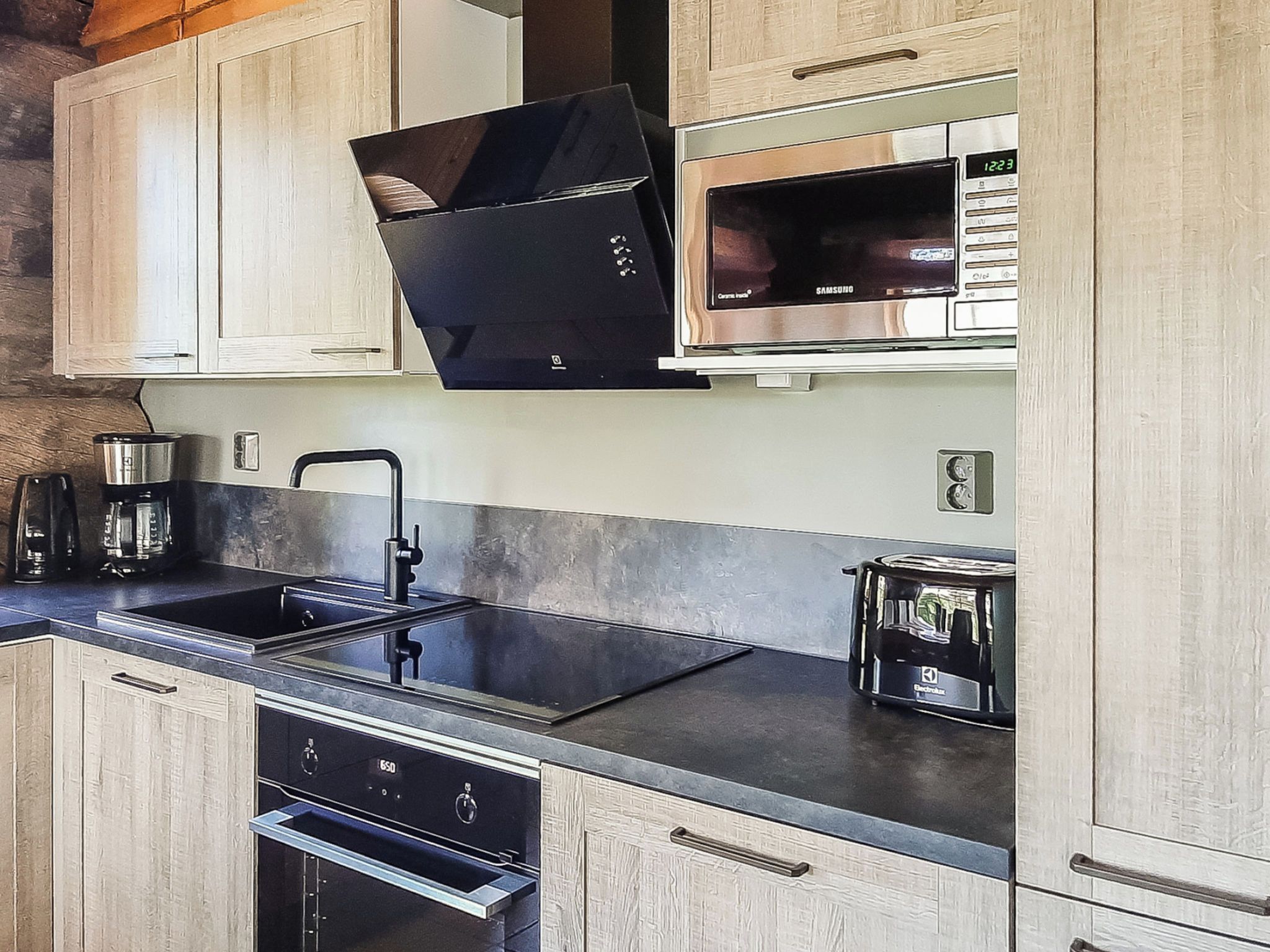 Een moderne keuken met een zwarte afzuigkap, roestvrijstalen apparatuur en houten keukenkastjes.