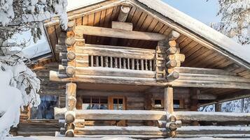 Une cabane en rondins dotée d’un balcon, entourée d’arbres couverts de neige.