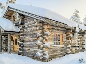 En timmerstuga med ett snötäckt tak och ett fönster med träpersienner.