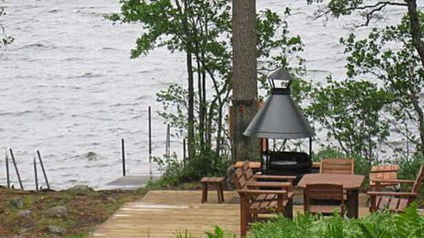 An outdoor seating area with a grill and a table, surrounded by trees and a body of water. - Vacation home 5816 by Interhome (Äänekoski)