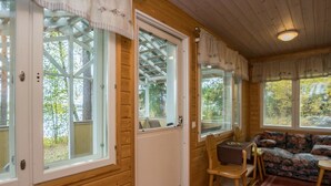 A cozy cabin interior with a wooden exterior, large windows, a sofa, and a dining table.