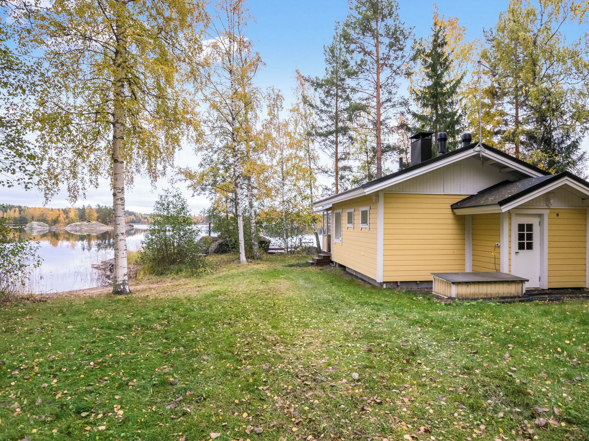 Ein gelbes Blockhaus mit Steg, umgeben von Bäumen und einem See.