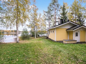 Keltainen mökki, jossa on laituri, ja sen ympärillä on puita ja järvi.