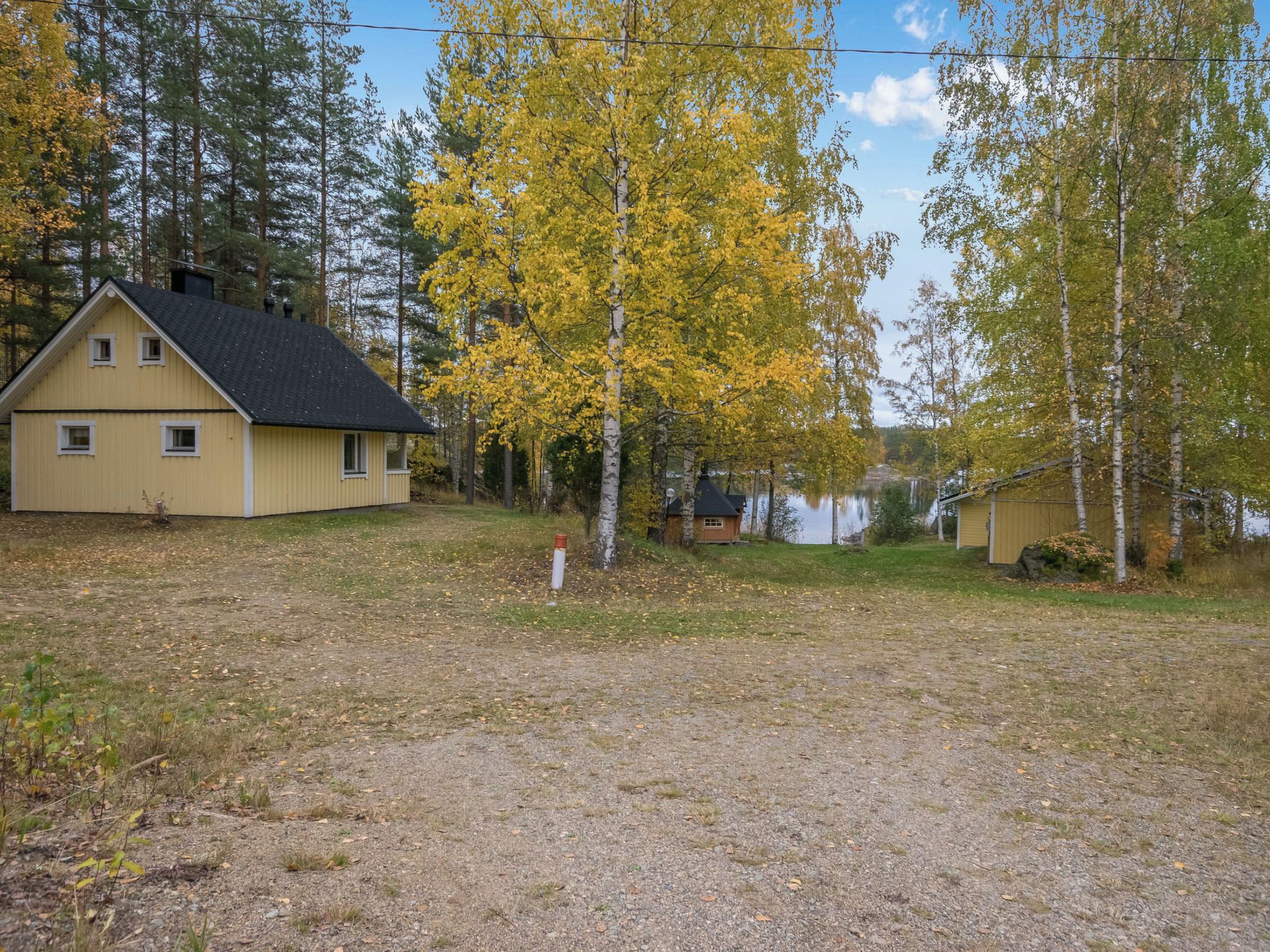 Une maison avec un toit en pente, une cour avec un chemin de gravier et un lac en arrière-plan.