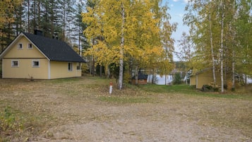 Une maison avec un toit en pente, une cour avec un chemin de gravier et un lac en arrière-plan.
