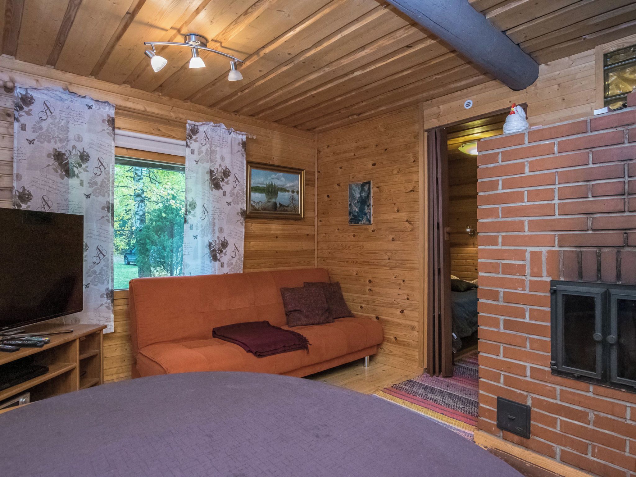 Une pièce chaleureuse avec un plafond en bois, un canapé, une télévision et une cheminée.