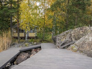 Ein Holzsteg führt zu einer Lodge, umgeben von Bäumen mit gelben Blättern.