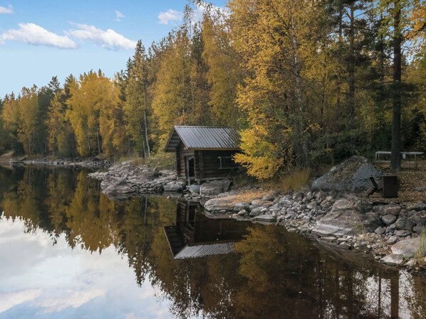 A cabin by a calm lake surrounded by autumn trees.