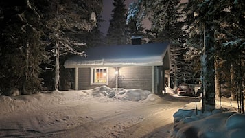 A cabin with a snow-covered ground, surrounded by trees.