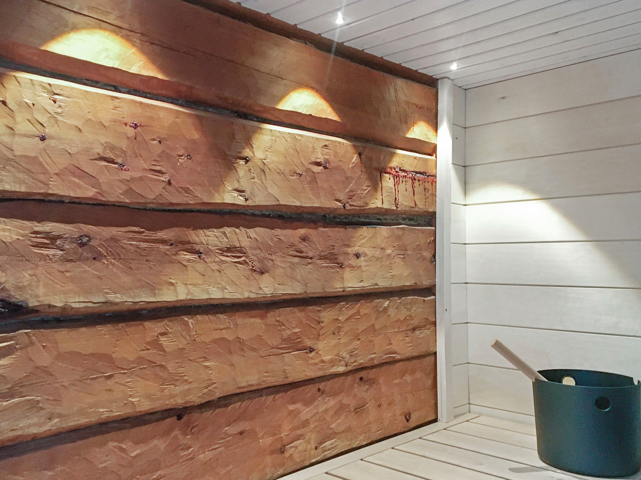 A room with wooden panel walls, a white ceiling, and a blue bucket on the floor.