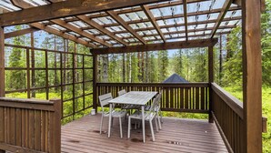 En træterrasse med et bord og stole, omgivet af gelænder og glaspaneler.