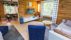Indretning i en hyggelig hytte med trævæg, spiseplads, tv og sofa.