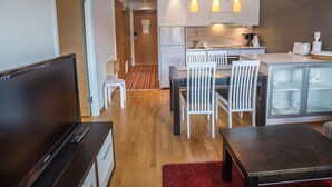 Eine moderne Küche mit weißen Schränken, eine Essecke mit weißen Stühlen und ein Fernseher im Wohnzimmer.