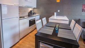Eine moderne Küche mit weißen Schränken, einem Bosch-Kühlschrank und einem Essbereich mit einem schwarzen Tisch und weißen Stühlen.