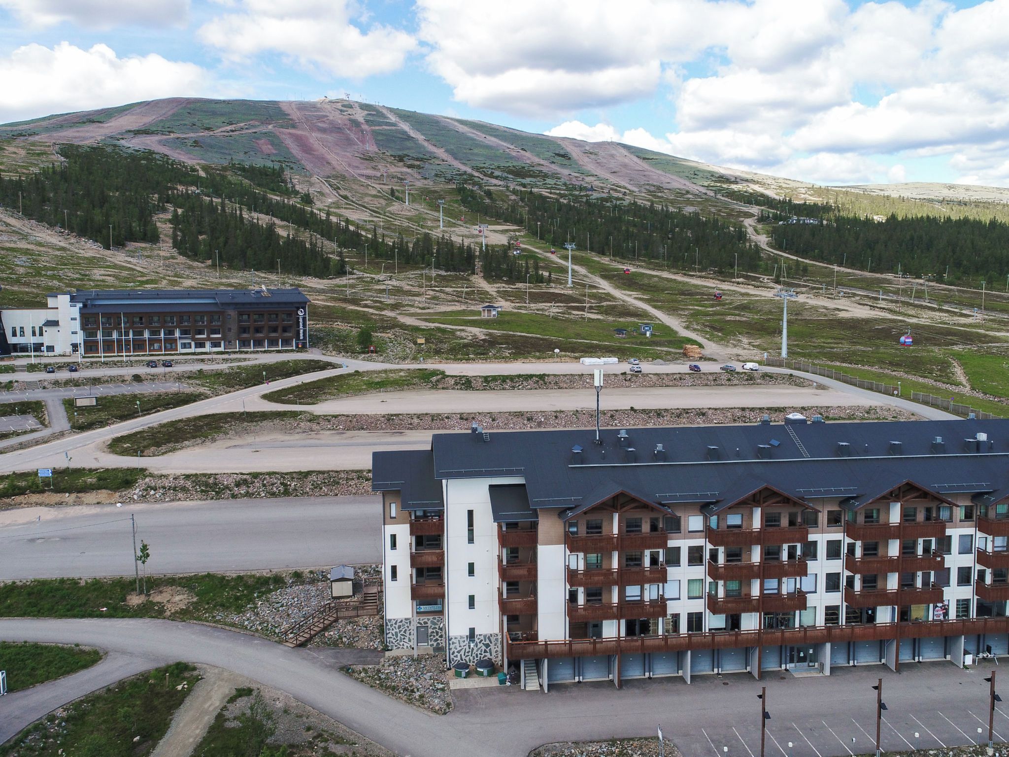 A multi-story hotel with a modern design, located in a mountainous area with a parking lot and a road leading to the entrance.