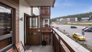 Ein Balkon mit Holzgeländern, einer Bank und Blick auf eine Straße mit Autos und Gebäuden im Hintergrund.