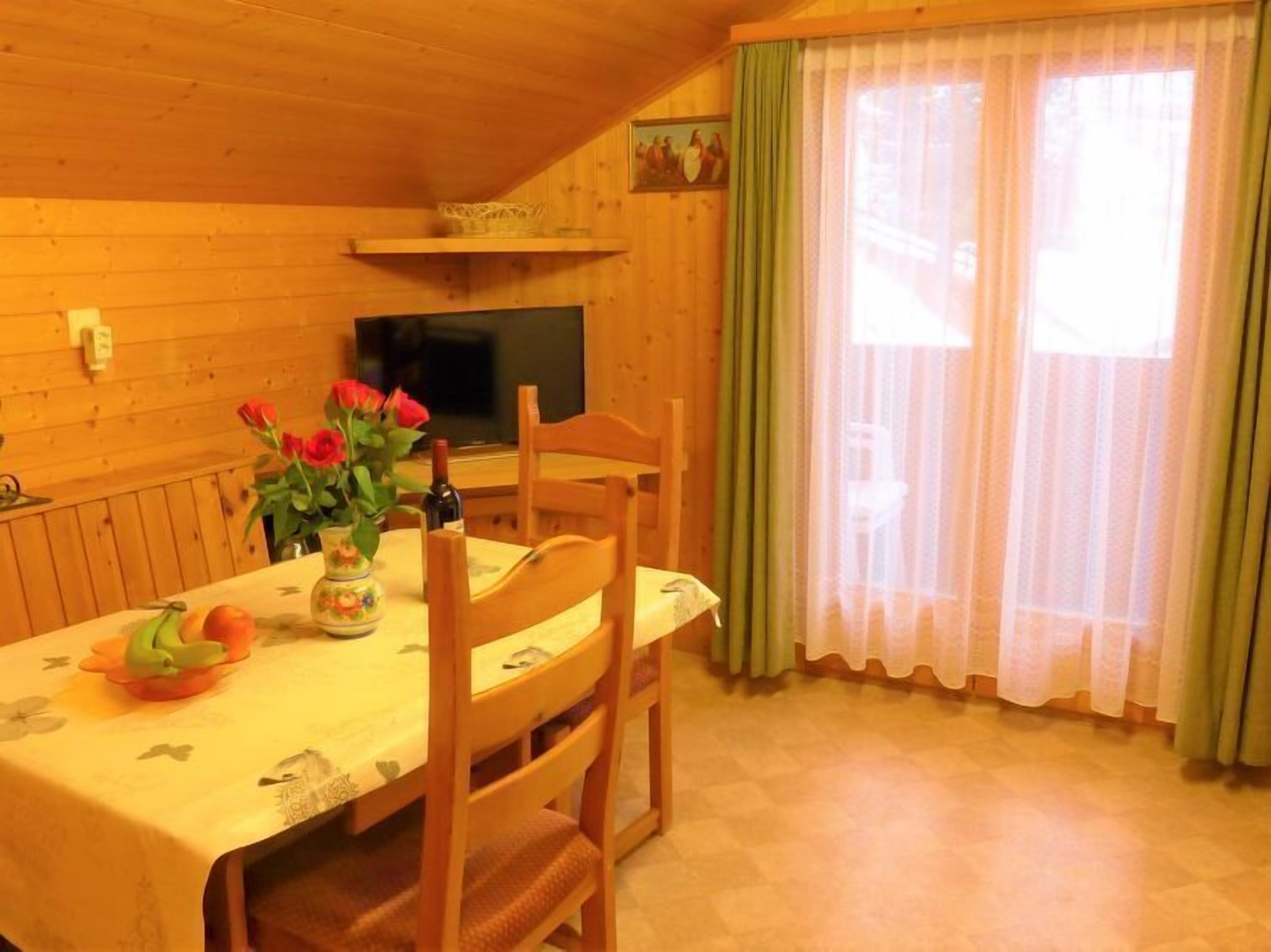 Een houten interieur met een eettafel gedekt voor twee personen, een televisie aan de muur en een raam met groene gordijnen.