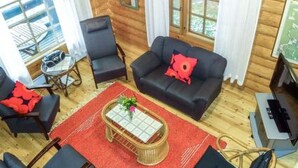 L’intérieur d’un chalet confortable, avec un salon comprenant un canapé noir, un coussin rouge, une table basse en bois et un tapis rouge.