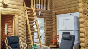 L’intérieur d’une cabane en rondins, avec un escalier en bois, deux chaises, une petite table et une cheminée.