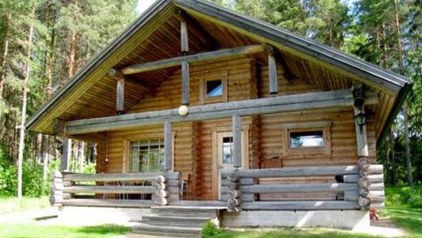 Une cabane en bois avec une véranda, une cheminée et une fenêtre.