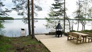 Une terrasse en bois au bord d’un lac, agrémentée d’un belvédère, de bancs et d’un barbecue.